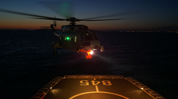 Ship-borne helicopter lands on helipad at night